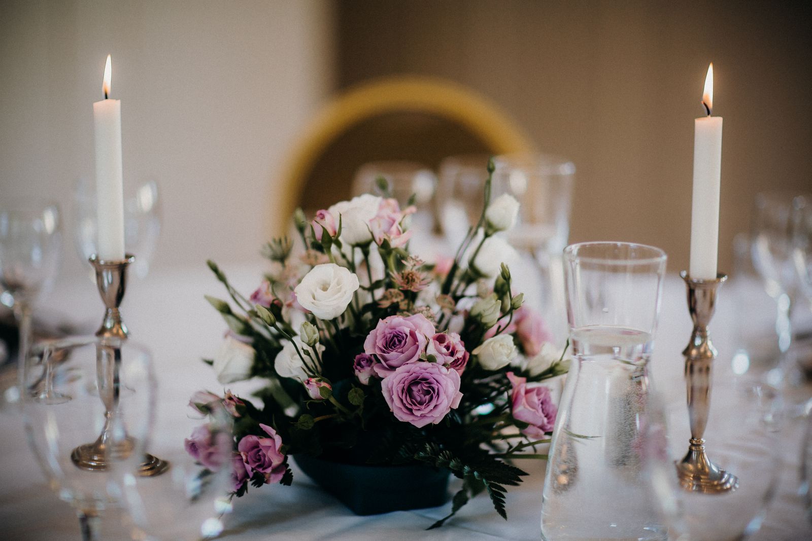 A low arrangement of pink and white roses between candlesticks on a set table