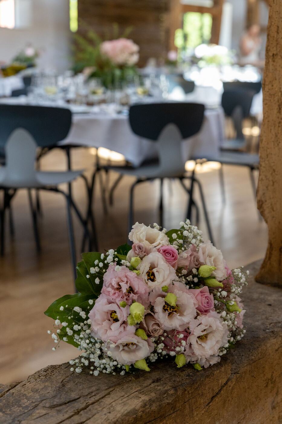 A pink and cream bridal bouquet resting on a wooden beam at a wedding venue