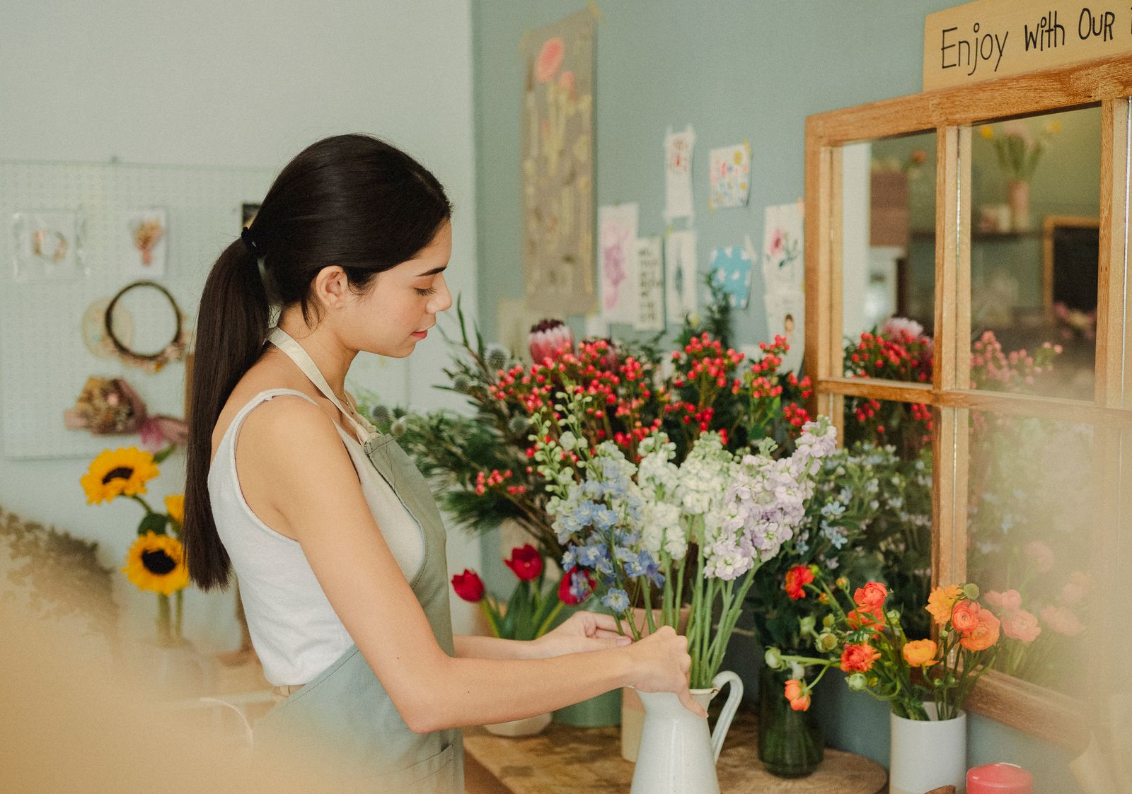 A florist arranging colorful stems into a pitcher on a workbench