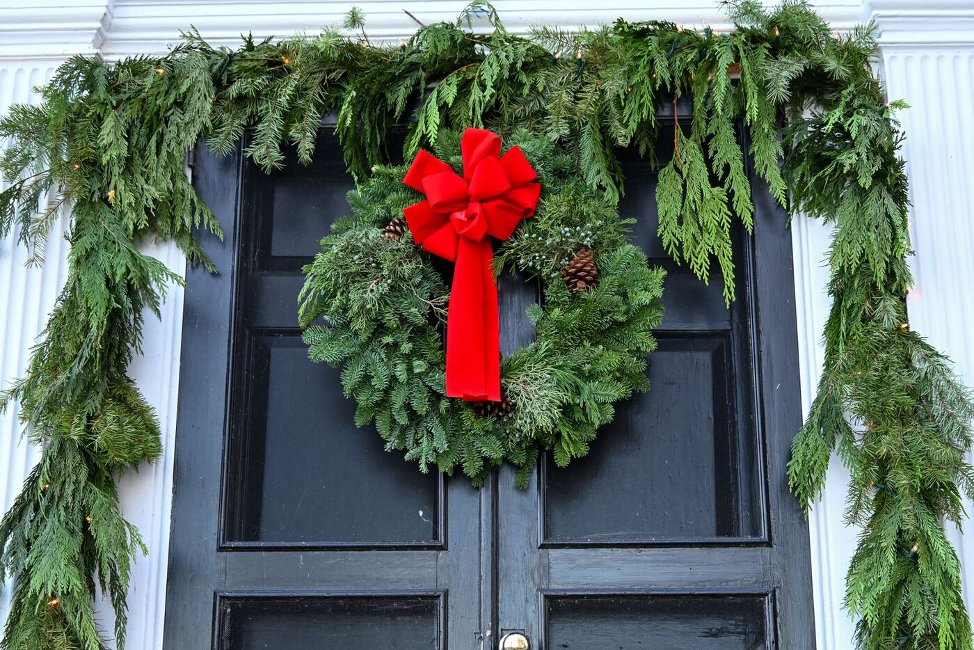 A round evergreen wreath with a red bow on a black door
